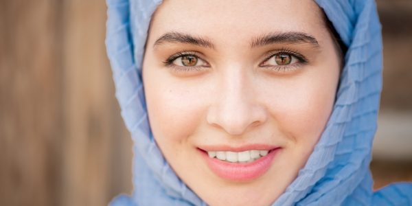 Face of young smiling Arabian female in blue hijab looking at you